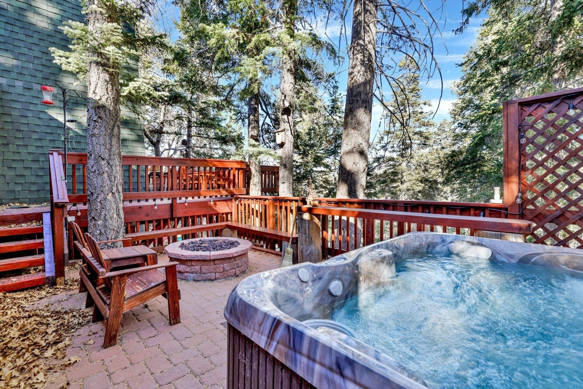 An outdoor hot tub area with a wooden deck, seating, and a fire pit.