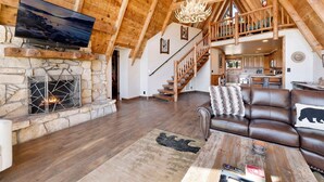 A spacious living area with a stone fireplace, wooden ceiling beams, a leather sofa, and a television mounted on the wall.