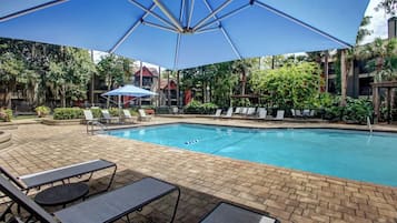 A swimming pool with lounge chairs and umbrellas, surrounded by greenery and buildings.