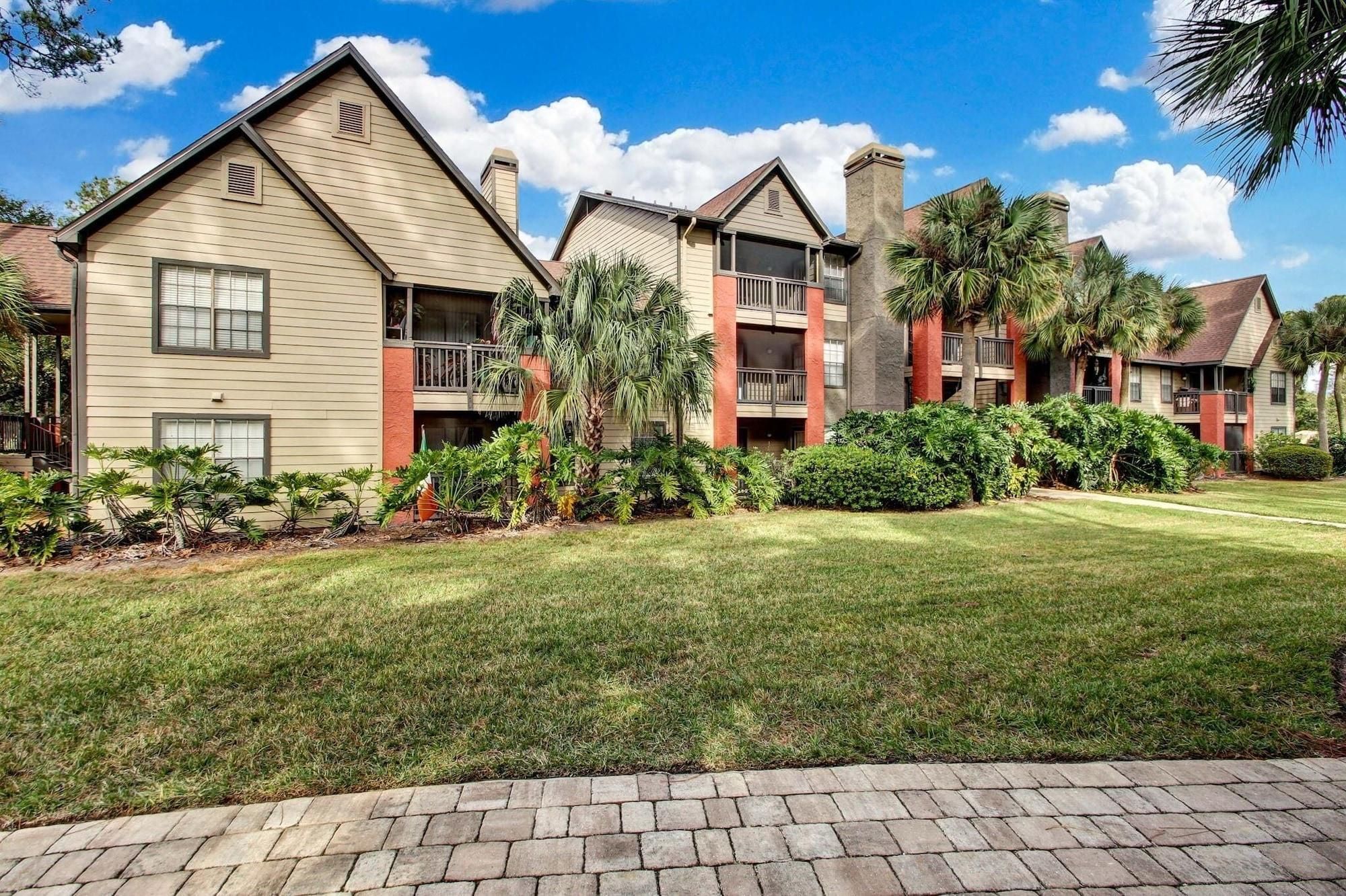 A row of two-story residential buildings with balconies, surrounded by well-maintained lawns and tropical plants.
