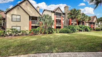 A row of two-story residential buildings with balconies, surrounded by well-maintained lawns and tropical plants.