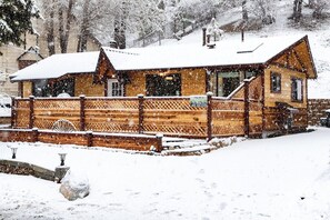 Una cabaña de madera con techo nevado y una terraza de madera.