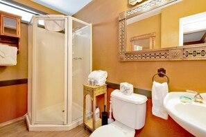 A bathroom with a glass-enclosed shower, a toilet, a sink, and a mirror with a decorative frame. - Club View Pines #2105 (Big Bear Lake)
