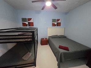 A room with bunk beds, a single bed, a ceiling fan, and two abstract paintings on the walls. - Puntilla Apartments No. 3 (Cataño)