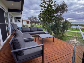 Une terrasse avec un canapé, des chaises et une table, offrant une vue sur une étendue d’eau et la verdure.