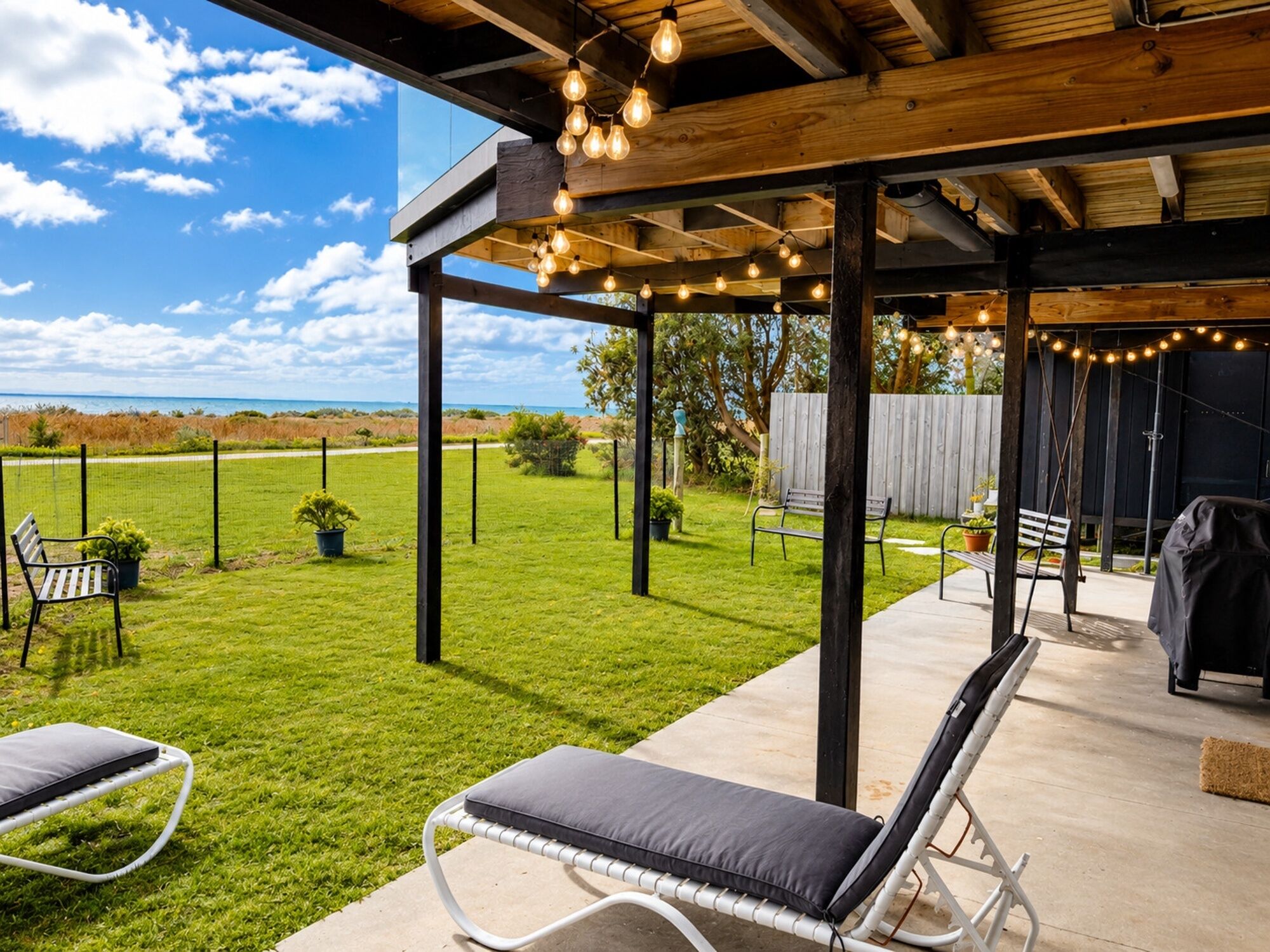 A covered outdoor patio with a view of a grassy yard and a wooden deck.
