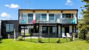 A modern two-story house with a balcony, large windows, and a fenced yard. - Coastal 3-Bed Haven With Panoramic Views (Portarlington)