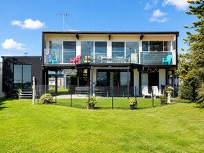 A modern two-story house with a balcony, large windows, and a fenced yard. - Coastal 3-Bed Haven With Panoramic Views (Portarlington)