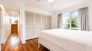 A bedroom with a bed, wooden flooring, a ceiling fan, and a window with curtains. - Coastal 3-Bed Haven With Panoramic Views (Portarlington)