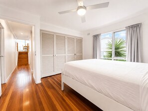 A bedroom with a bed, wooden flooring, a ceiling fan, and a window with curtains. - Coastal 3-Bed Haven With Panoramic Views (Portarlington)