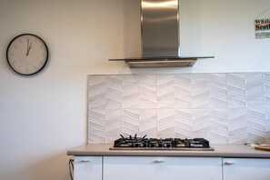 Une cuisine équipée d’une cuisinière à gaz, d’une hotte en acier inoxydable et d’une horloge murale.