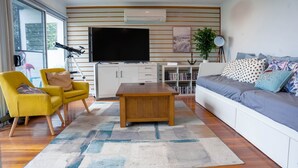 A modern living room with a flat-screen TV, yellow armchairs, a wooden coffee table, and a grey sofa with patterned cushions. - Coastal 3-Bed Haven With Panoramic Views (Portarlington)