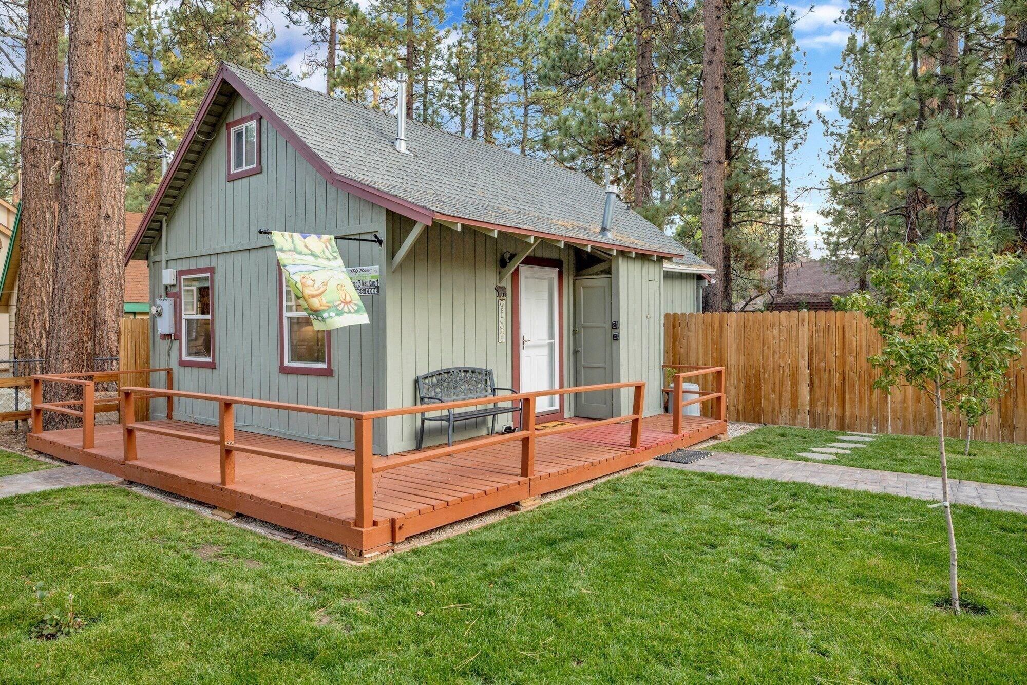 A small cabin with a porch, a welcome sign, and a wooden fence.