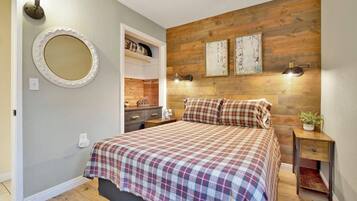 A bedroom with a wooden headboard, a bed with plaid bedding, a nightstand, a mirror, and a shelf with decorative items.