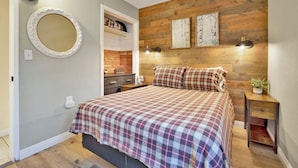A bedroom with a wooden headboard, a bed with plaid bedding, a nightstand, a mirror, and a shelf with decorative items. - Beary Cozy Cabin #2315 (Big Bear Lake)