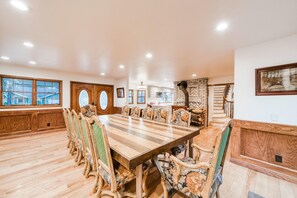 A spacious dining area with a long wooden table and ornate chairs, large windows, and a fireplace. - Bears Palace Chalet #2008 (Big Bear Lake)
