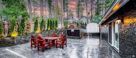 Un patio con una mesa y sillas de piedra, rodeado de árboles altos y un muro de piedra.