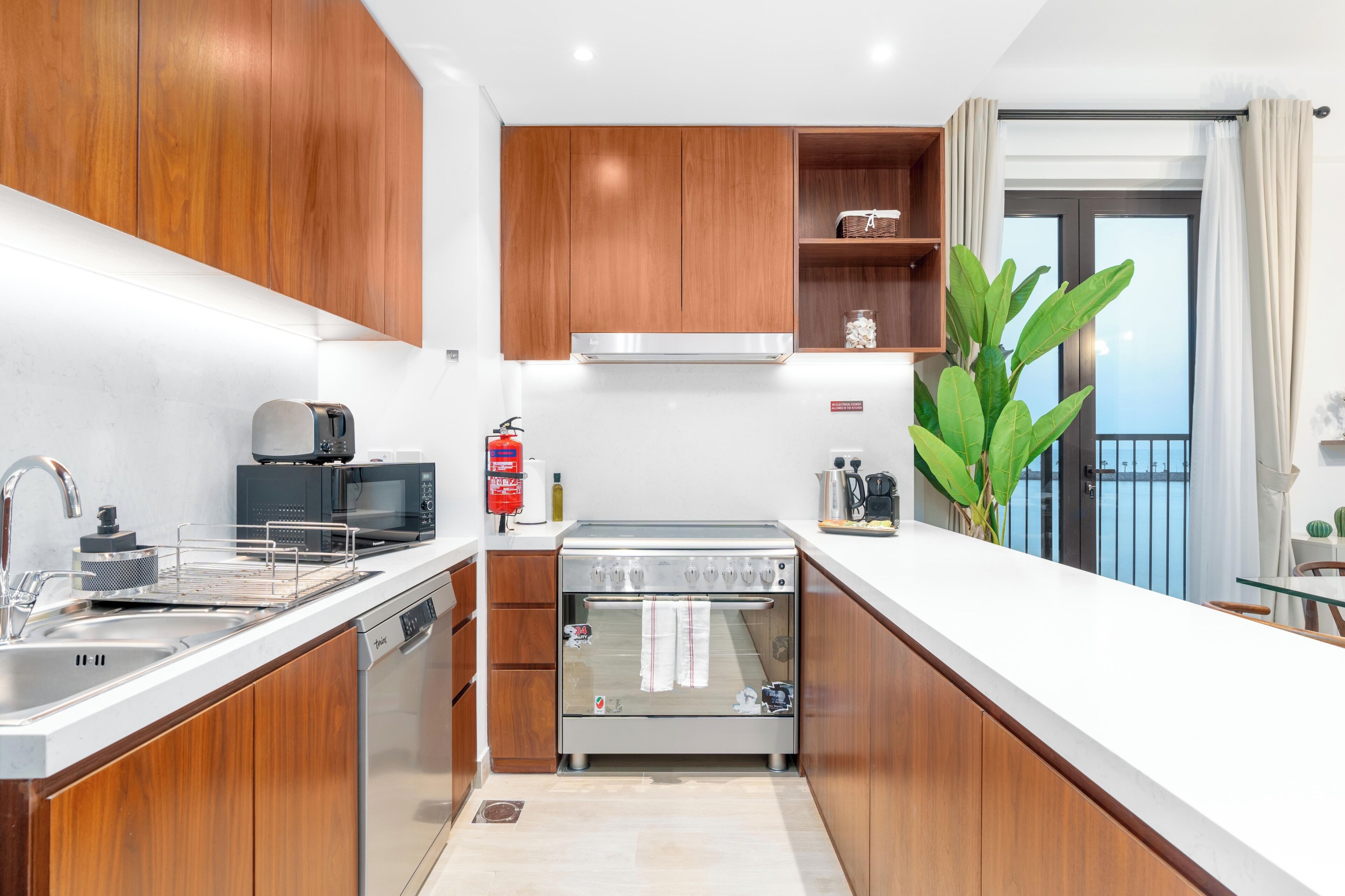 A modern kitchen with wooden cabinets, stainless steel appliances, and a view of the sea through a balcony.