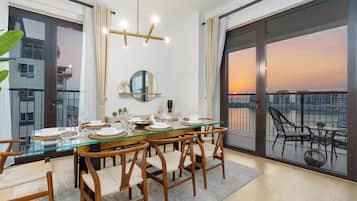 Un comedor con mesa de vidrio, sillas de madera y vistas al atardecer a través de grandes ventanales.