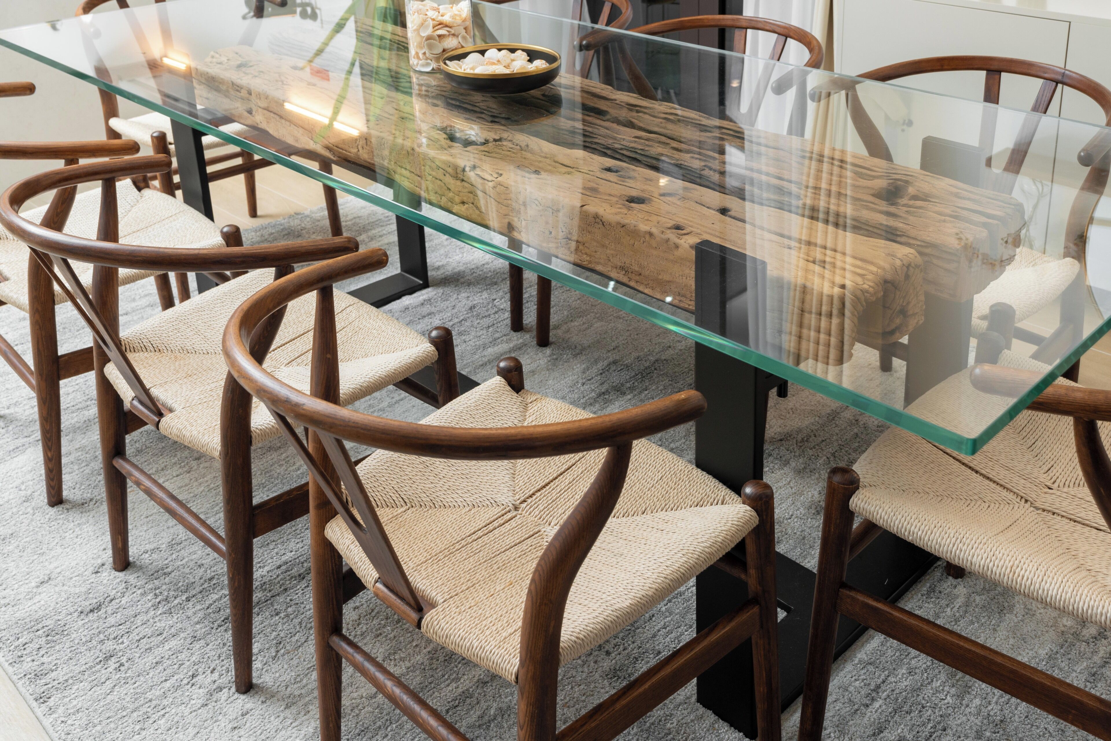 Une table à manger avec un plateau en verre, entourée de chaises en bois dont les assises sont en osier tressé.