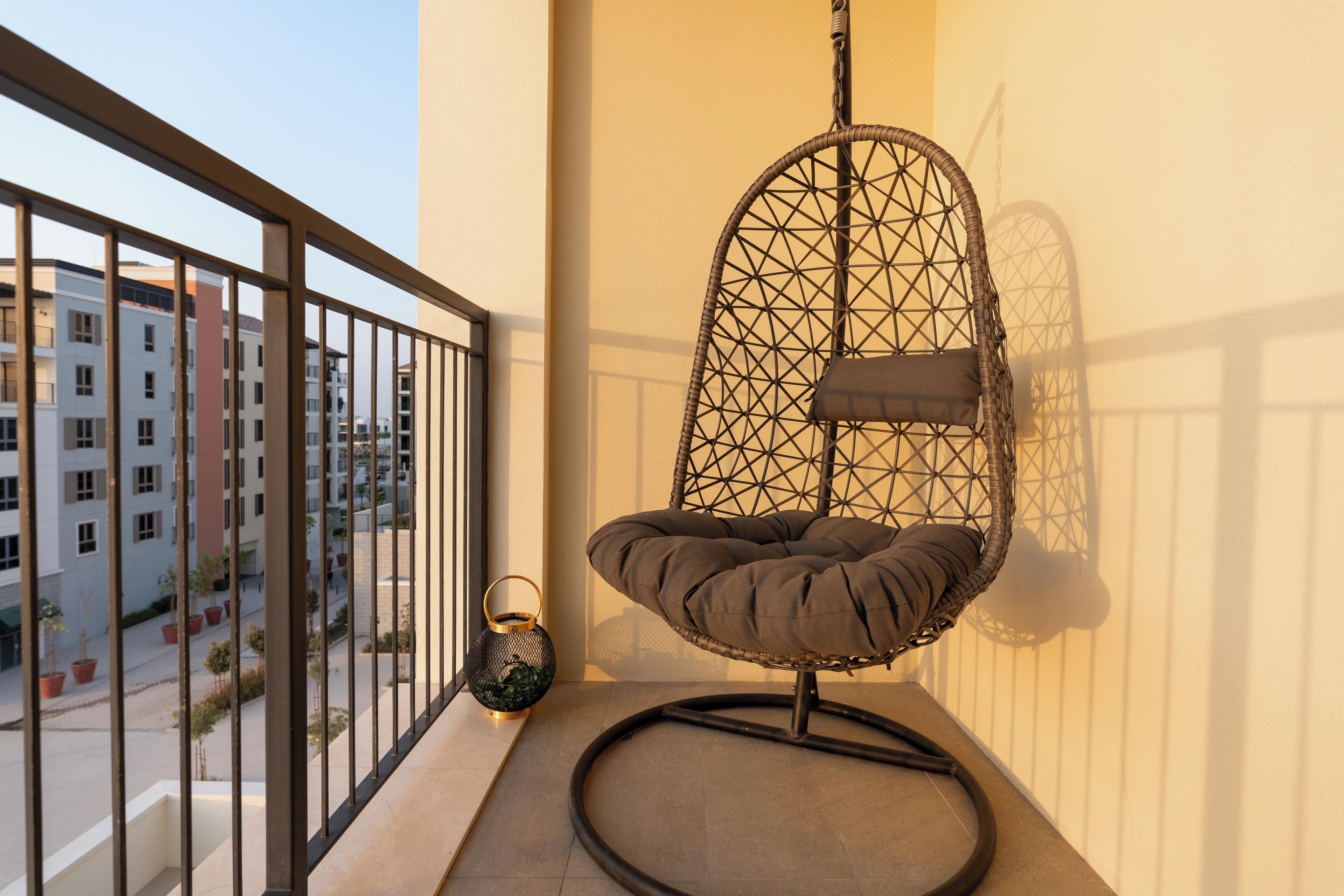 A balcony with a hanging chair, a lantern, and a view of buildings.