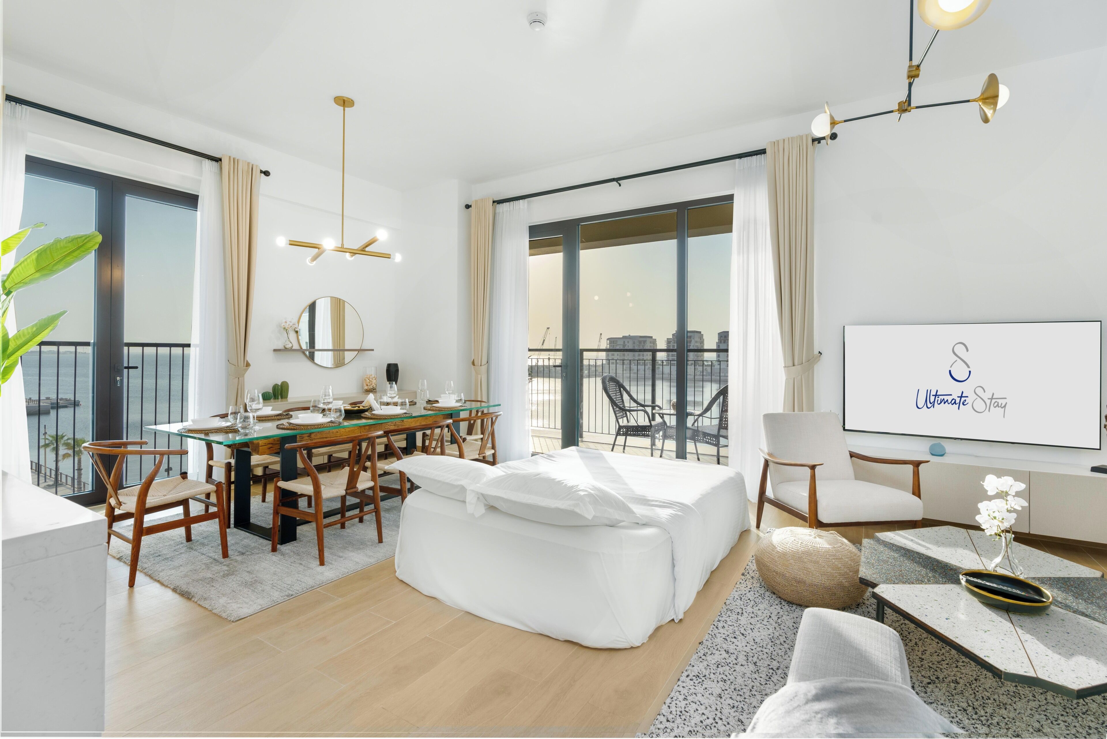 A modern hotel room with a balcony, a dining area, a bed, and a TV.