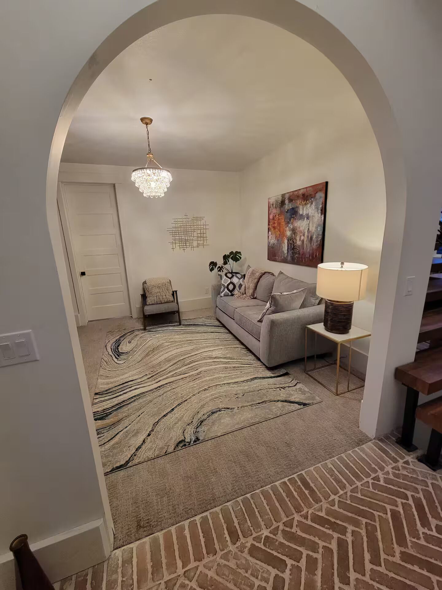 A living room with a grey sofa, a patterned rug, a chandelier, and a painting on the wall.