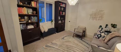 A living room with a bookshelf, a sofa, a chair, a rug, and a chandelier.