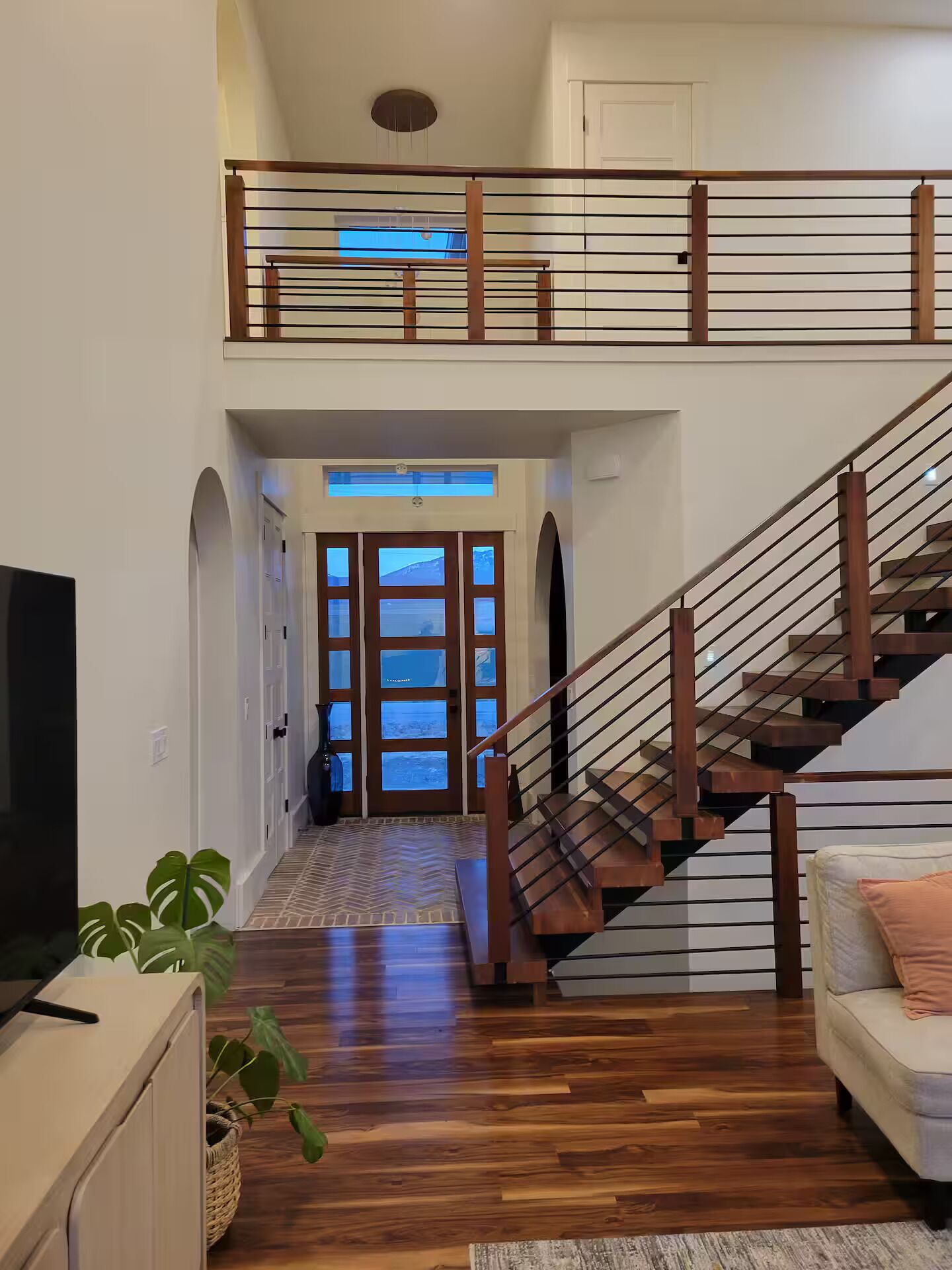 Un vaste espace de vie agrémenté d’un escalier en bois, d’un téléviseur à écran plat et d’un canapé.
