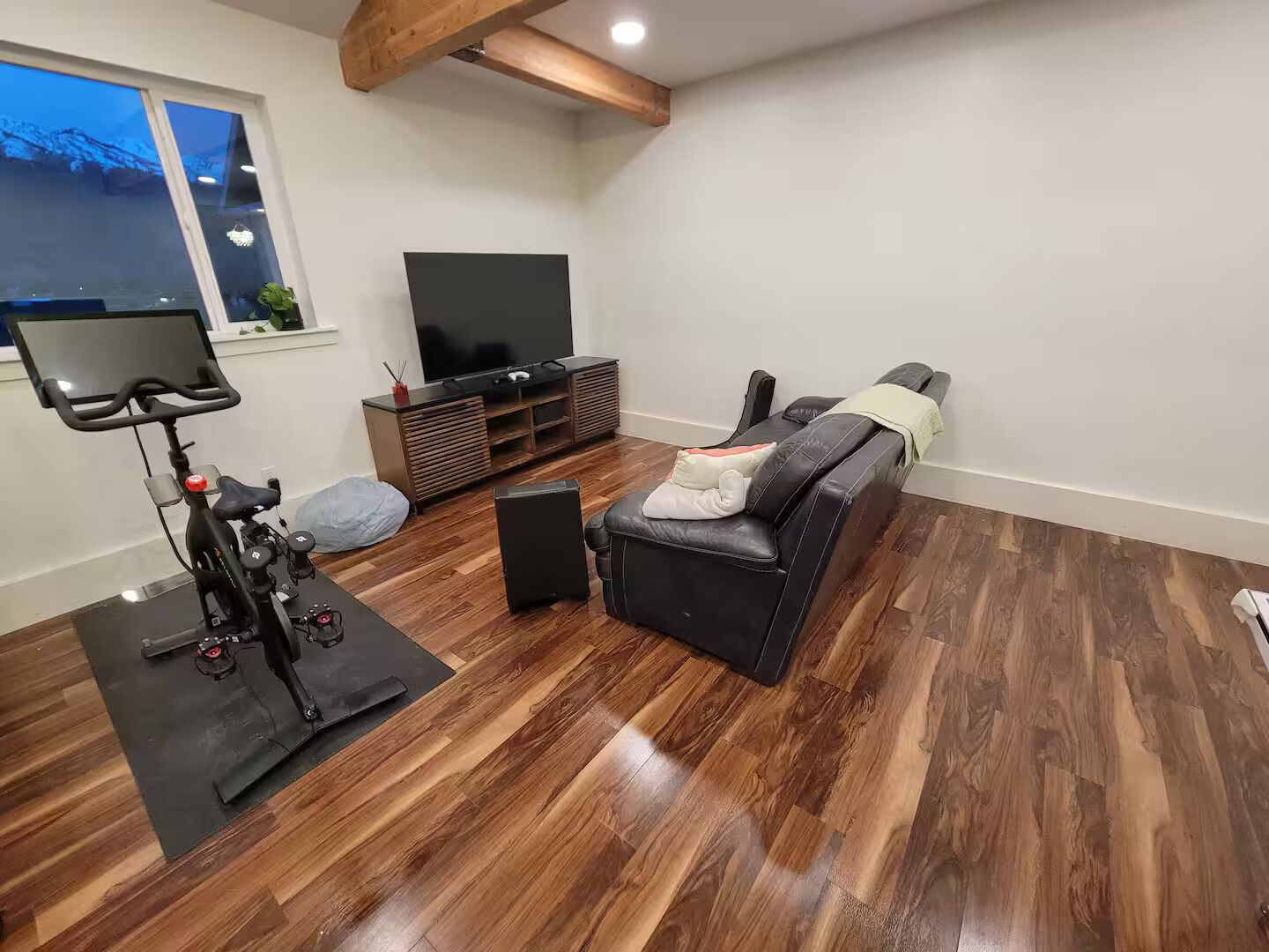 A living room with a wooden floor, a black sofa, a TV stand, and a stationary bike.