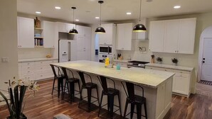 Cozinha moderna com armários brancos, uma ilha central com banquetas e iluminação pendente.