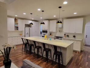 A modern kitchen with white cabinetry, a central island with bar stools, and pendant lighting. - Beautiful, spacious country home in Cache Valley with views (Wellsville)