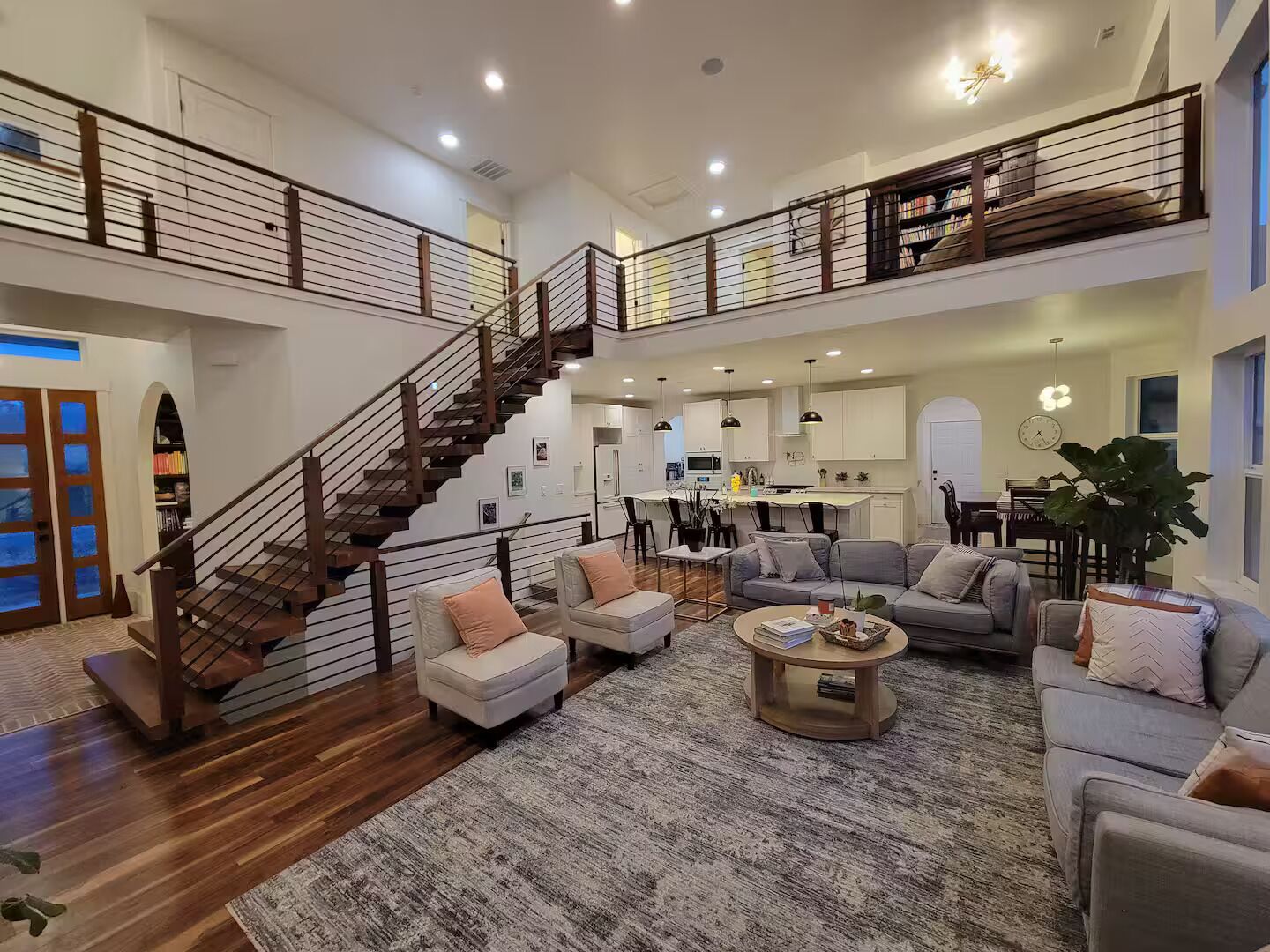 A spacious living area with a staircase, multiple seating options, and a kitchen in the background.