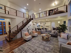 Un amplio salón con escalera, diversas opciones de asiento y una cocina al fondo.