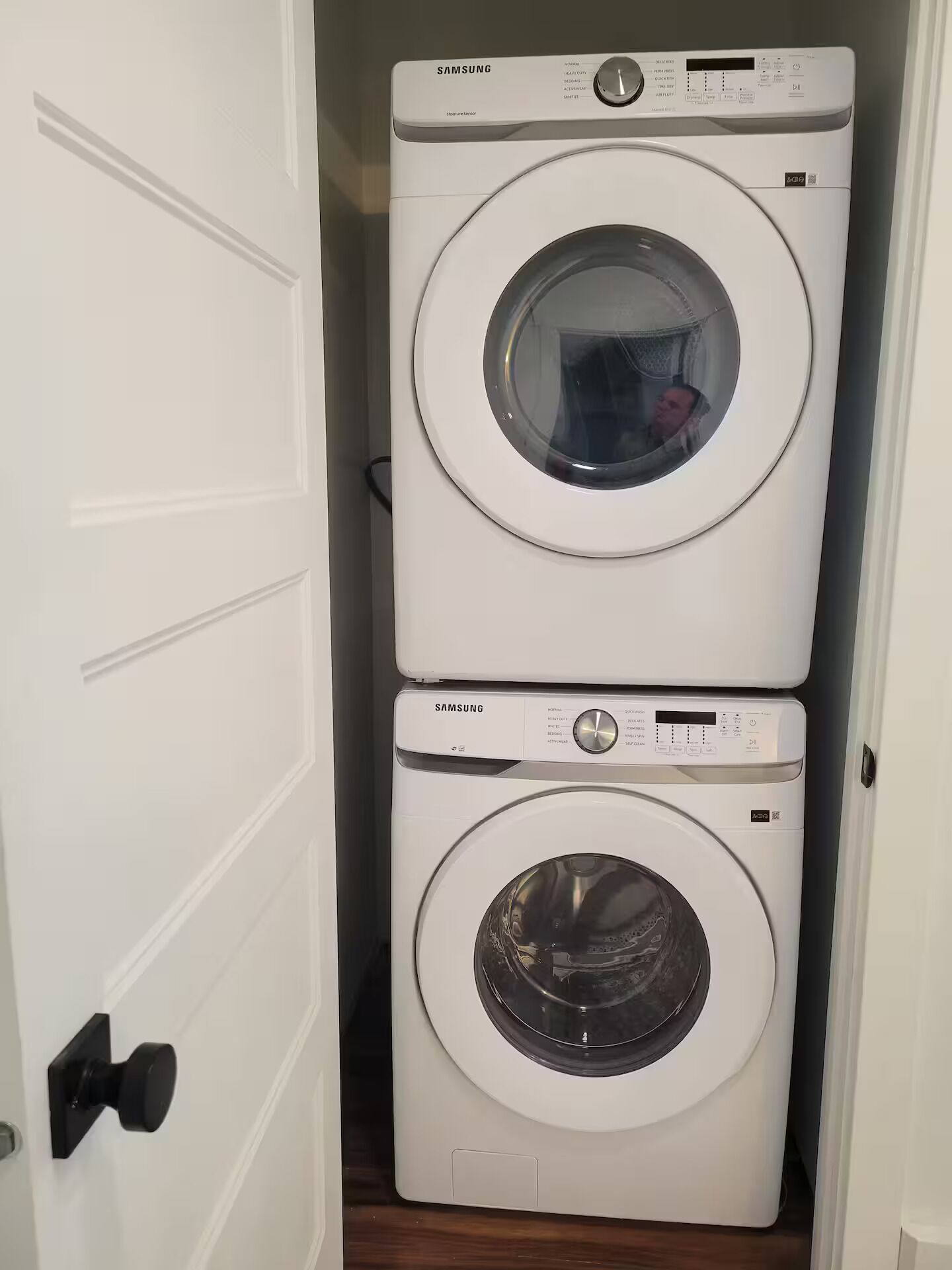 En hvid væg med en dør, der er åben på klem, og som giver adgang til et vaskeri med vaskemaskine og tørretumbler.