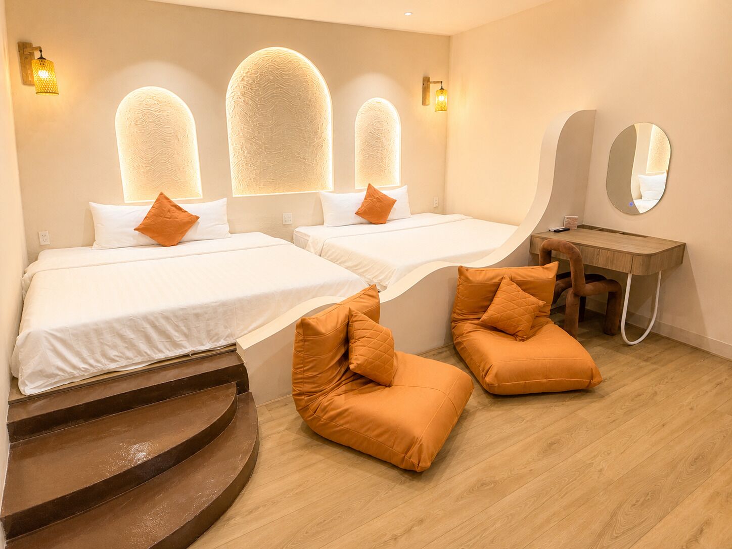 A hotel room with two beds, a desk, a mirror, and a staircase.