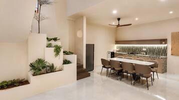 Uma cozinha moderna com ilha integrada, área de jantar com uma mesa comprida e cadeiras, e escada decorada com plantas.