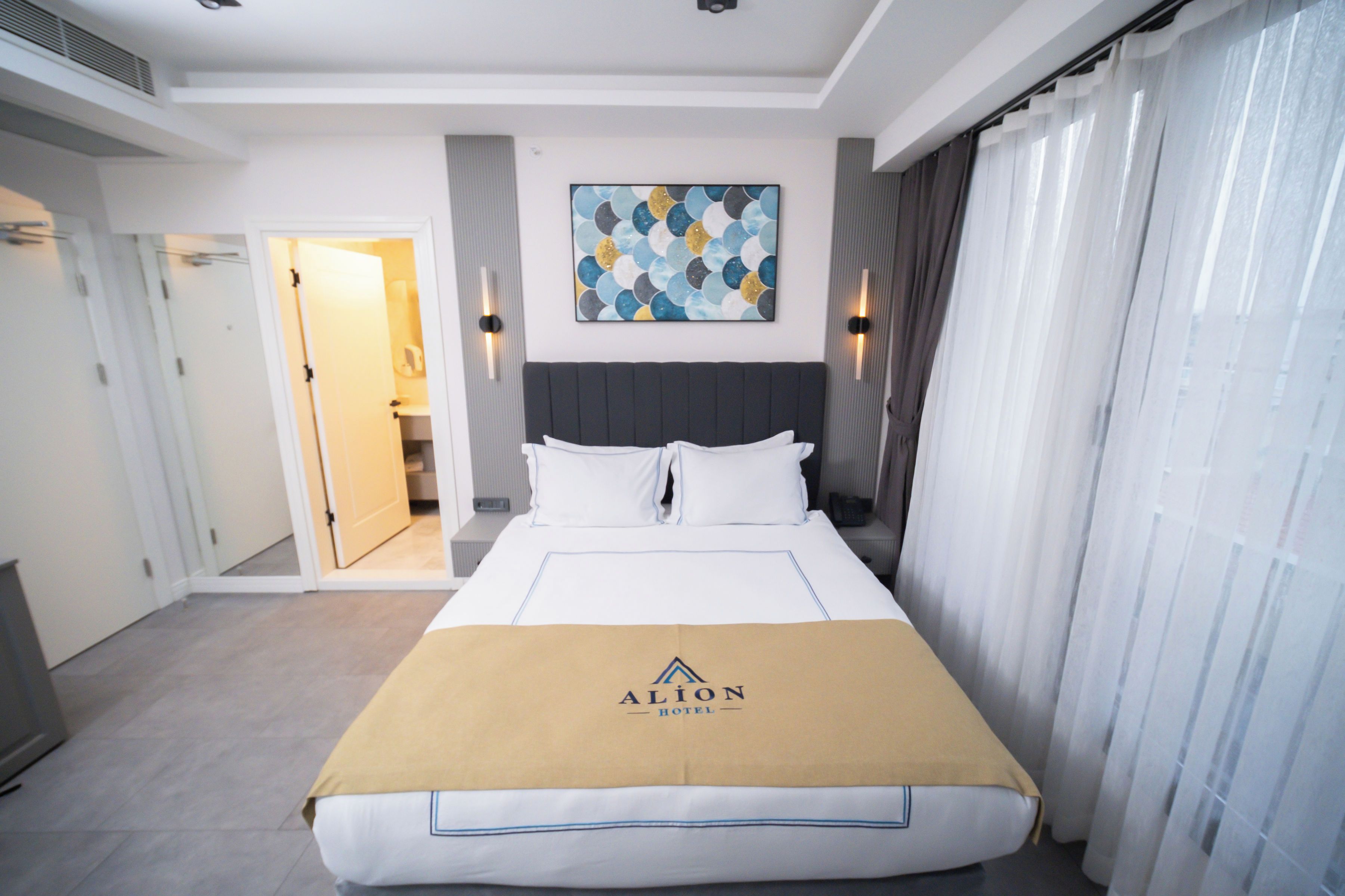 Une chambre d’hôtel avec un lit, une tête de lit, un tableau au mur et une porte donnant sur une autre pièce.