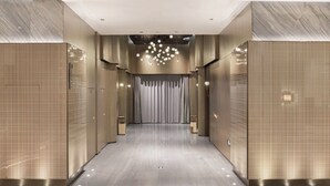 A modern hotel corridor with a central chandelier, recessed lighting, and a patterned wall design.