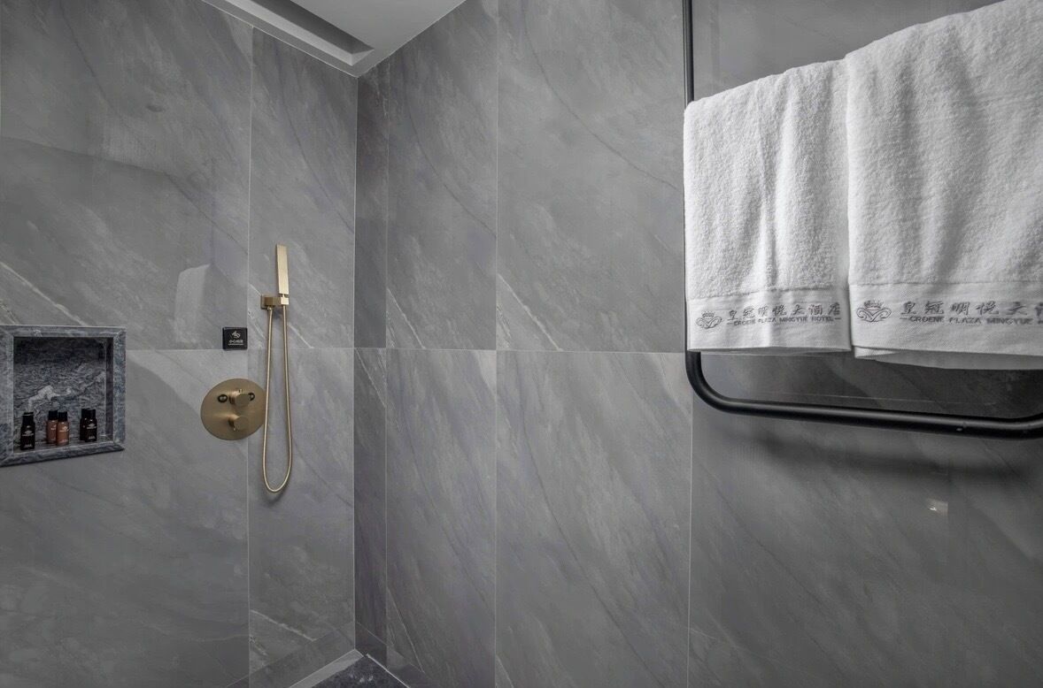 Un baño moderno con baldosas de mármol gris, mampara de vidrio y un perchero con dos toallas.