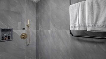 Un baño moderno con baldosas de mármol gris, mampara de vidrio y un perchero con dos toallas.