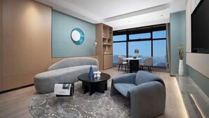 A modern living room with a sofa, armchair, coffee table, and a dining area with a view.