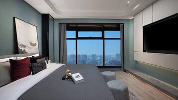 A modern bedroom with a large bed, a flat-screen TV mounted on the wall, and a city view through the window.