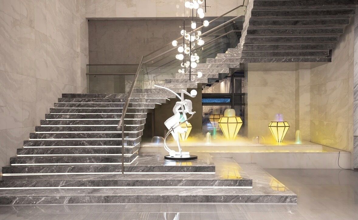 A modern interior with a marble staircase, a sculpture, and a unique lighting fixture.