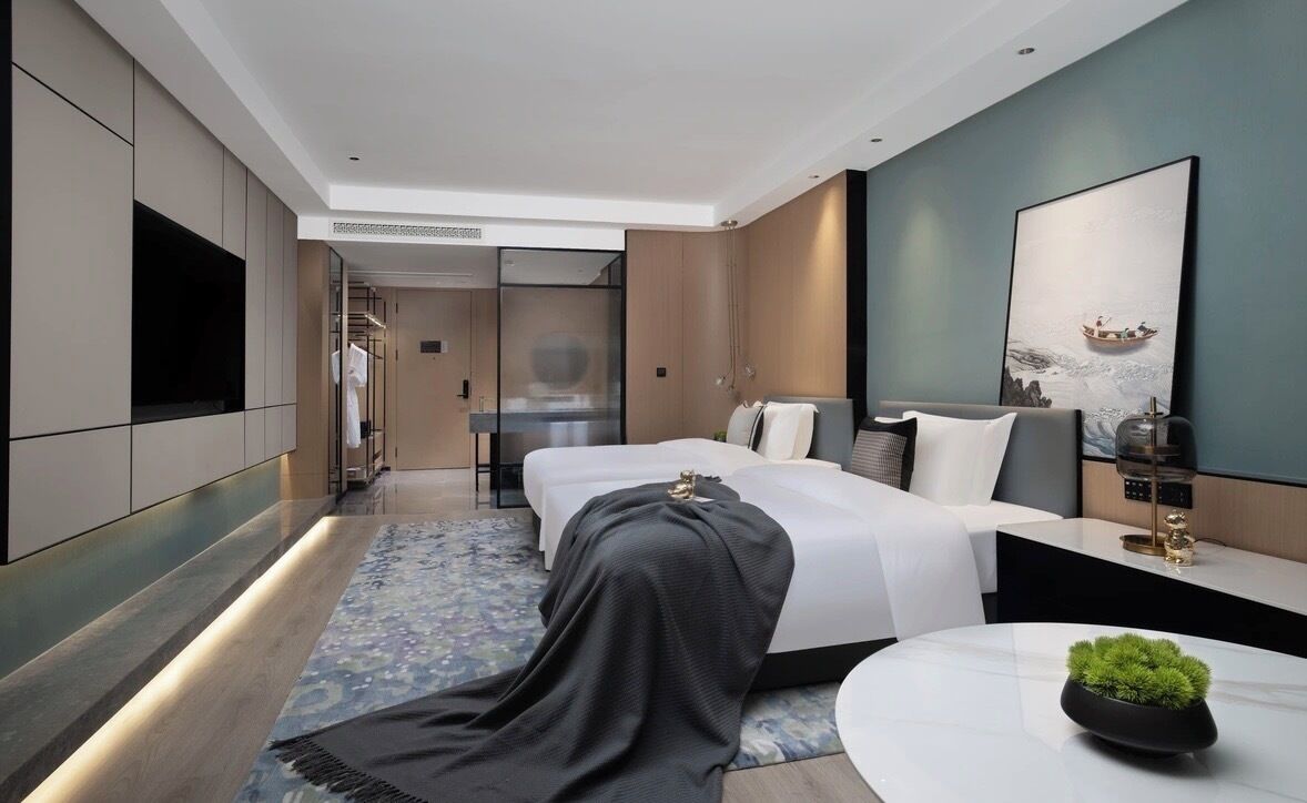 Une chambre d’hôtel moderne, équipée d’un lit, d’une table de chevet et d’une grande fenêtre.
