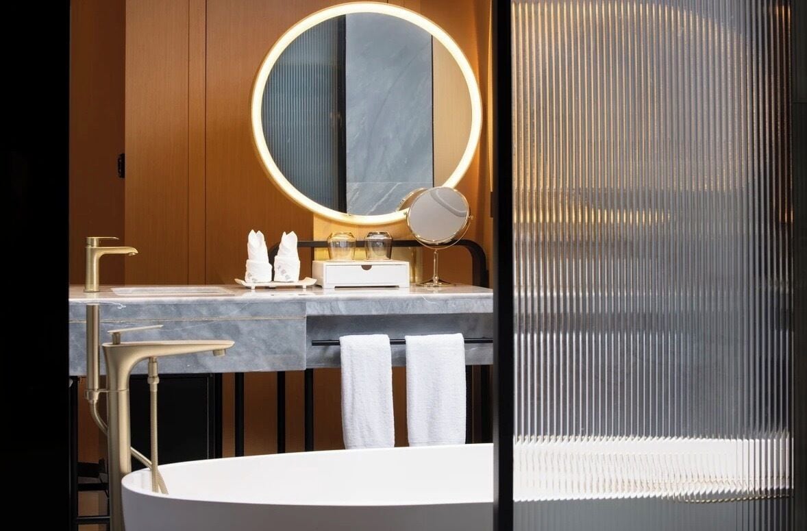 A modern bathroom with a round mirror, a vanity with a marble countertop, and a bathtub.