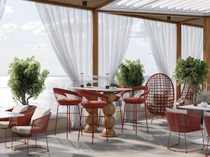 An outdoor dining area with a table and chairs, potted plants, and a view of the sea.
