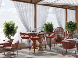 Un área de comedor al aire libre con una mesa, sillas, plantas en macetas y vista al mar.