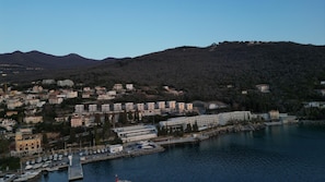 A coastal town with a marina, buildings, and a mountainous backdrop.