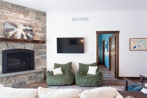 A living room with a stone fireplace, two green bean bag chairs, a flat-screen TV, and a framed map on the wall. - Secluded Lakefront Retreat on 14 Acres with Private Boathouse & Firepit (St. Germain)